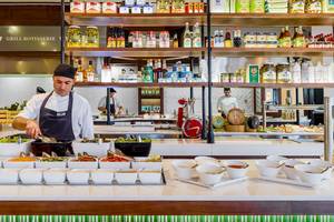 Koch im H10 Rubicon Palace bereitet Gerichte in der Grill Rotisserie zu, mit Zutaten und Utensilien um ihn herum.