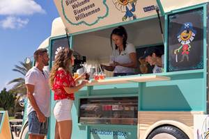 Zwei Gäste stehen an der Eiswagen-Theke von H10 Rubicon Palace, eine Frau serviert ihnen Getränke.
