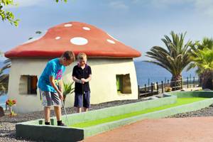 Zwei junge Jungs spielen Golf auf einem Pilzhaus-Golfplatz mit Meer im Hintergrund