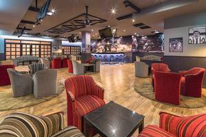 Lobby-Lounge-Bereich des H10 Rubicon Palace Hotels mit rot und grau gestreiften Sesseln und Tischen auf hölzerne Boden.