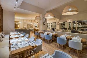 Innenraum des H10 Rubicon Palace Restaurants mit blauen Stühlen und Holztischen.