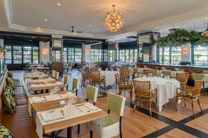 Innenbereich des H10 Rubicon Palace Restaurants mit Holztischen, Stühlen und einer großen Kronleuchter.