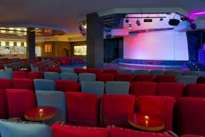 Innenansicht des H10 Rubicon Palace Hotels mit einem großen Saal, roten und grauen Stühlen, und einer Bühne.