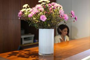 Eine weiße Vase mit bunten Blumen steht auf einem hölzernen Tisch.