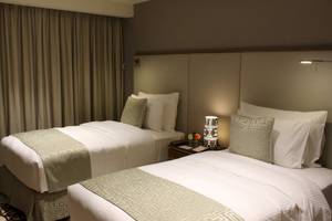 Zwei Betten mit cremefarbenen Bezügen und weißen Kissen im Hotelzimmer des Grand Millennium Muscat.