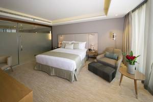 Hotelzimmer im Grand Millennium Muscat mit Doppelbett, Sesseln und Tisch mit Blumen.
