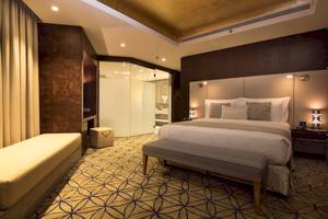 Innenansicht eines eleganten Schlafzimmers im Grand Millennium Muscat Hotel, mit großem Bett, gepolstertem Nachttisch und luxuriösem Badezimmer.