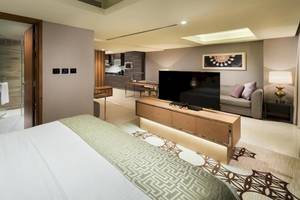 Innenansicht einer Suite im Grand Millennium Muscat mit Bett, Fernseher, Sofa und Dusche