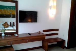 Innenansicht eines Hotelzimmers mit Fernseher, Spiegel, Nachttisch und Bank.