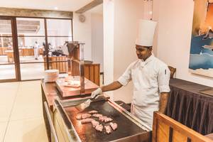 Koch in einem weißen Kochmütze, der Fleisch auf einem Grill in einem Hotel kocht.