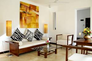 Wohnzimmer im Goldi Sands Hotel mit weißer Couch, schwarzen und weißen Kissen, Glastisch und Lampe.