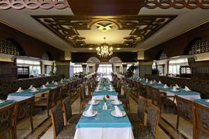 Restaurant im Adalya Bliss Hotel mit gedeckten Tischen und einer langen Tafel in der Mitte.