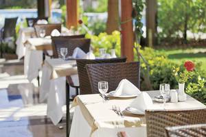 Restauranttisch im Freien im Adalya Bliss Hotel, elegant gedeckt mit Pflanzen im Hintergrund.