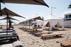 Mann geht an Sonnenliegen am Strand des Ikones Seafront Luxury Suites Hotels vorbei