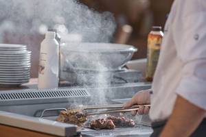 Ein Grillmeister brät Fleisch auf einem Grill im Cretan Dream Resort & Spa.
