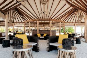 Strandlounge im Drift Thelu Veliga Retreat mit runden Sofas und Tischen auf weißem Sand.