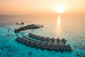 Luftaufnahme des Drift Thelu Veliga Retreats mit Wasserbungalows und Steg am Sonnenuntergang