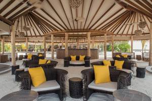 Loungebereich im Drift Thelu Veliga Retreat mit gelben Kissen und Korbstühlen.