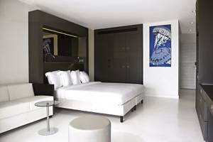 Modernes Zimmer im Papagayo Beach Hotel & Resort Curaçao mit weißem Bett, grauen Möbeln und blauem Wandbild.