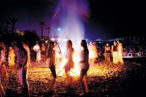 Menschen feiern um ein großes Feuer auf dem Strand des Terrace Beach Resorts bei Nacht.
