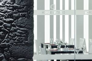 Innenansicht des Restaurants im Dimitra Beach Hotel & Suites mit schwarzen und weißen Tischplatten und weißen Stühlen.