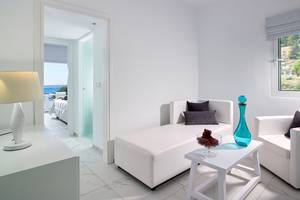 Innenansicht einer Suite im Dimitra Beach Hotel mit weißem Interieur, Schlafbereich und Wohnzimmerbereich.