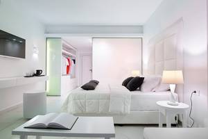 Ein modernes Schlafzimmer im Dimitra Beach Hotel & Suites mit weißen Wänden, einem großen Bett und Nachttischen.