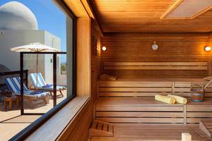 Innenansicht der Sauna im Seaside Sandy Beach Hotel mit Holzbänken, Fenster und Sonnenschirm.