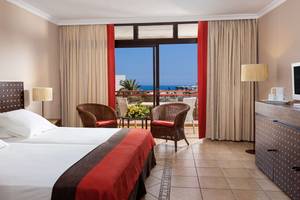 Doppelzimmer mit Meerblick im Seaside Sandy Beach Hotel, mit zwei Betten, zwei Korbstühlen und einem großen Fenster.
