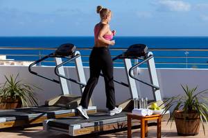 Frau läuft auf einem Laufband auf der Terrasse mit Blick auf das Meer.