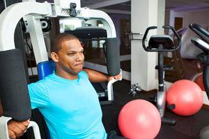 Mann im Fitnessstudio, der an einem Gerät arbeitet, umgeben von roten Gymnastikbällen.