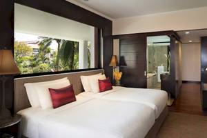 Doppelzimmer im Anantara Riverside Bangkok Resort mit zwei Betten, roten Kissen und einer Aussicht auf den Garten