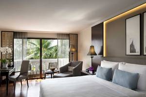 Schlafzimmer im Anantara Riverside Bangkok Resort mit großem Bett, Kissen und Blick auf den Garten.