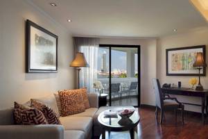 Wohnbereich des Anantara Riverside Bangkok Resorts mit Sofa, Tisch, Schreibtisch und Balkon.