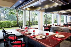 Innenbereich des Restaurants im Anantara Riverside Bangkok Resort mit roten Stühlen und Tischen, großen Fenstern und Blick auf Gärten