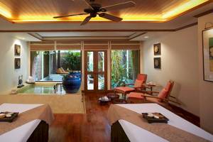 Massageraum im Anantara Riverside Bangkok Resort mit zwei Massagetischen, Blick auf einen Außenpool und Garten.
