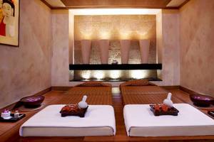 Behandlungsraum im Anantara Riverside Bangkok Resort mit zwei Massageliegen, gerahmten Bildern und Ambientbeleuchtung.