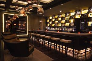 Barbereich im Mövenpick Hotel Jumeirah Beach mit gepolsterten Stühlen und beleuchteten Regalen.