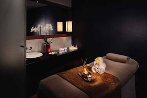 Spa-Behandlungsraum im Mövenpick Hotel Jumeirah Beach mit Tisch, Kerzen, Handtüchern und Pflanzen.