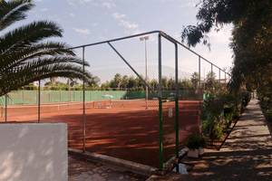 Tennisplatz im Atlantica Marmari Beach Hotel, umzäunt mit Pflanzen und Bäumen.