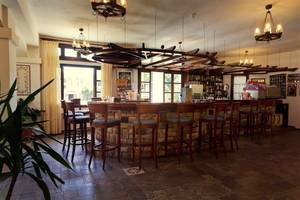 Innenansicht der Bar im Atlantica Marmari Beach Hotel mit Steinmauer und Holzbarhockern.