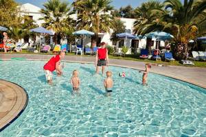 Kinder schwimmen im Pool im Atlantica Marmari Beach Hotel mit Sonnenschirmen und Liegestühlen im Hintergrund.