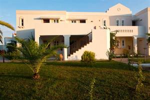 Außenansicht des Atlantica Marmari Beach Hotels mit grünem Rasen und Palme.