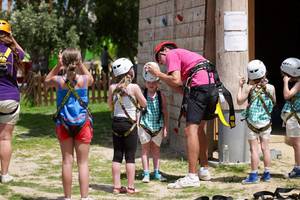 Kinder an einer Kletterwand im Atlantica Holiday Village Kos, alle tragen Sicherheitshelme und werden von einem Mann instruiert.