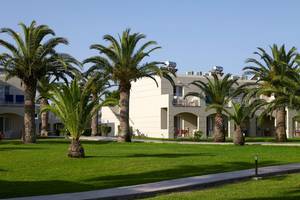 Außenbereich des Atlantica Holiday Village Kos mit Gebäuden, Palmen und Rasen.