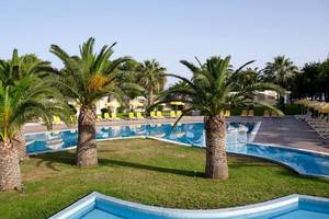 Außenpool des Atlantica Holiday Village Kos mit Palmen und Sonnenliegen.