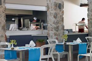 Restaurant des Atlantica Holiday Village Kos mit blauen Tischdecken und Köchen im Hintergrund.