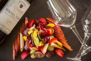 Obstsalat mit Weingläsern und einer Flasche Wein auf schwarzem Hintergrund