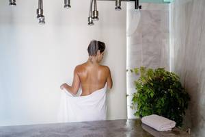 Frau im Kontokali Bay Resort & Spa steht unter einer Dusche und hält einen weißen Bademantel.