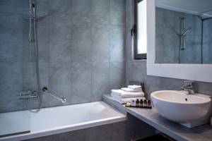 Badezimmer im Kontokali Bay Resort & Spa mit Badewanne, Handtuchstaender, Waschbecken und Spiegel.